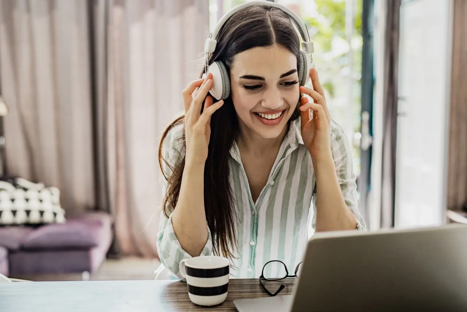 A student in headphones smiling during a live online class on their laptop